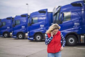 A female truck driver standing in front of a row of trucks while talking on the phone