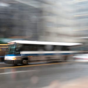 A blue and white bus driving quickly on a road